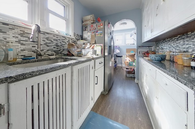 kitchen with arched walkways, a sink, decorative backsplash, white cabinets, and stainless steel refrigerator with ice dispenser