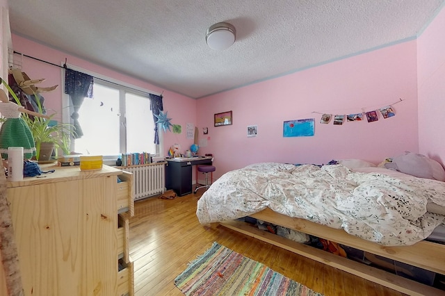 bedroom featuring a textured ceiling, radiator heating unit, and light wood finished floors