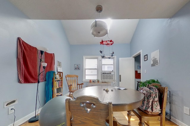 dining room featuring light wood-type flooring, radiator heating unit, cooling unit, baseboards, and vaulted ceiling