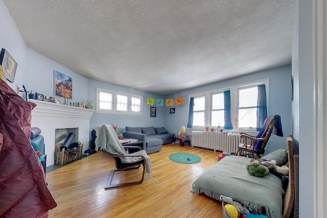 living room featuring hardwood / wood-style floors, radiator, a fireplace with flush hearth, and a textured ceiling