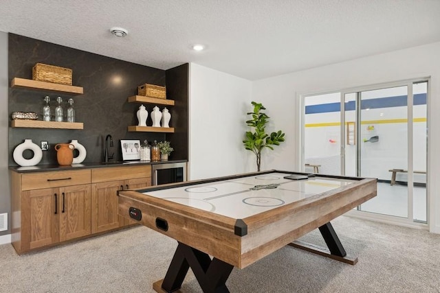 game room with light colored carpet, wine cooler, a sink, a textured ceiling, and indoor wet bar