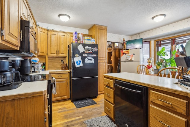 kitchen with light countertops, light wood finished floors, black appliances, and a textured ceiling