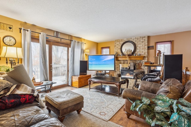 living room with a brick fireplace, plenty of natural light, a textured ceiling, and wood finished floors