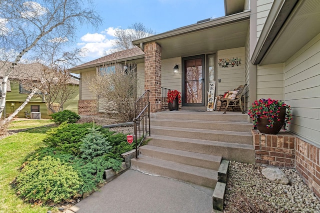 entrance to property featuring a porch and brick siding