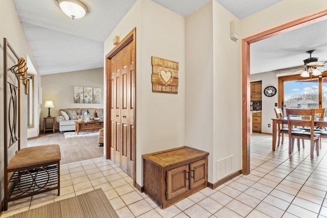 hall featuring light tile patterned floors, vaulted ceiling, a textured ceiling, and visible vents