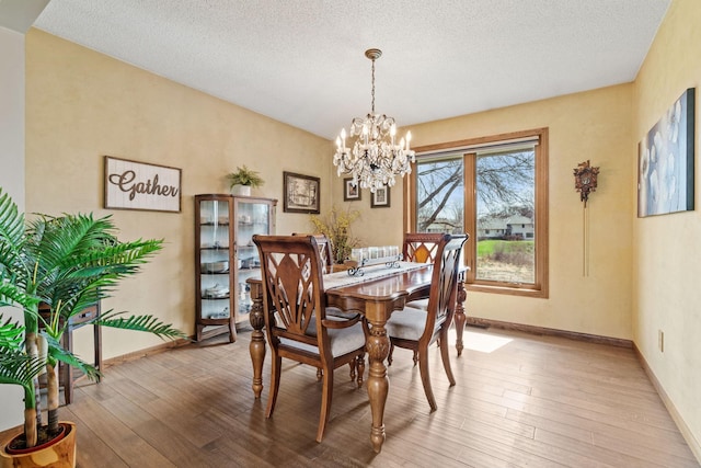 dining area featuring baseboards, a textured ceiling, wood finished floors, and a chandelier