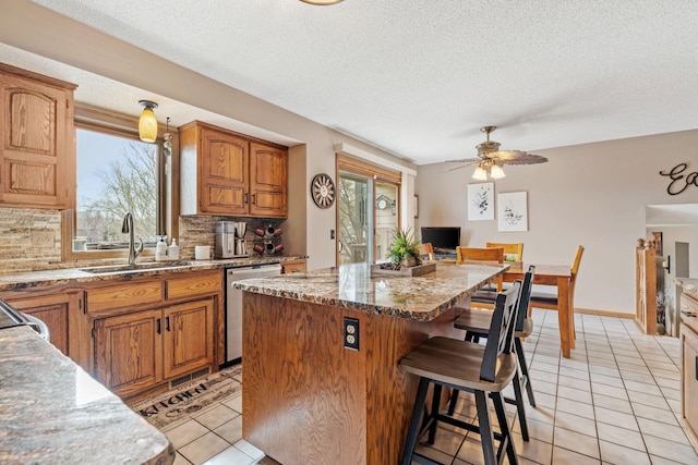 kitchen with a kitchen island, stainless steel dishwasher, a sink, light tile patterned floors, and a breakfast bar
