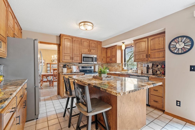 kitchen with light stone countertops, a kitchen bar, tasteful backsplash, a sink, and appliances with stainless steel finishes