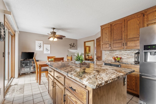 kitchen with decorative backsplash, ceiling fan, stainless steel refrigerator with ice dispenser, a center island, and light tile patterned floors