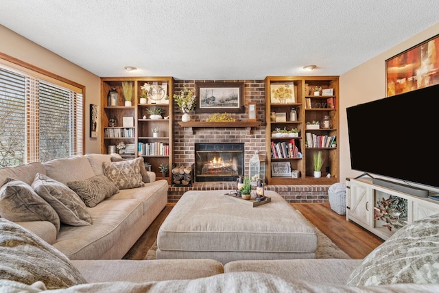 living area with a textured ceiling, a brick fireplace, and wood finished floors