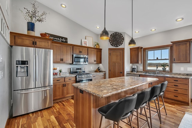 kitchen with light wood finished floors, a kitchen island, stainless steel appliances, and a sink