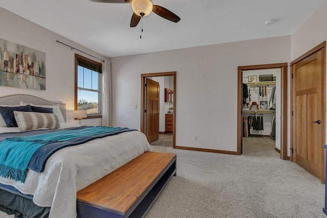 bedroom featuring light carpet, ensuite bath, baseboards, ceiling fan, and a spacious closet