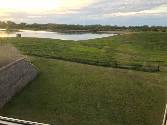 yard at dusk with a rural view, fence, and a water view