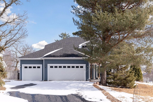 view of front facade featuring an attached garage, driveway, roof with shingles, and fence