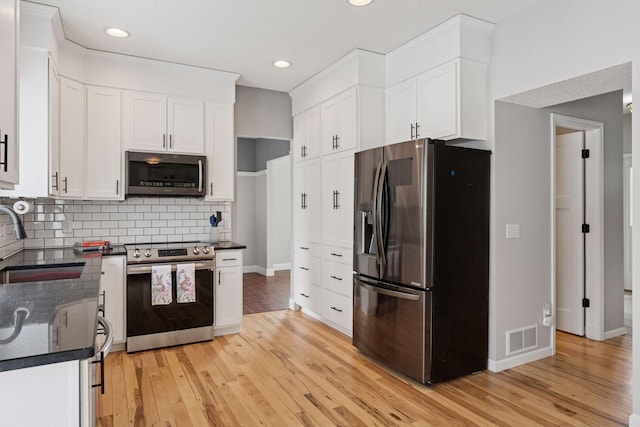 kitchen with light wood-style flooring, a sink, tasteful backsplash, stainless steel appliances, and white cabinets