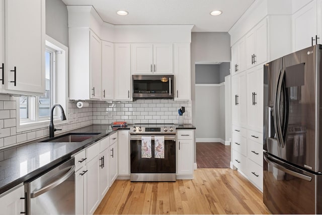 kitchen with dark stone countertops, light wood finished floors, a sink, stainless steel appliances, and white cabinetry