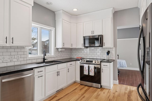 kitchen with a sink, dark countertops, white cabinetry, light wood-style floors, and appliances with stainless steel finishes