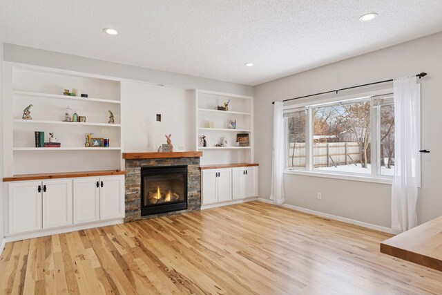 unfurnished living room featuring light wood-style floors, built in shelves, a textured ceiling, and a fireplace