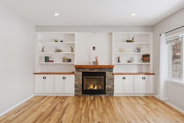 unfurnished living room featuring a stone fireplace, baseboards, light wood-style floors, and built in features