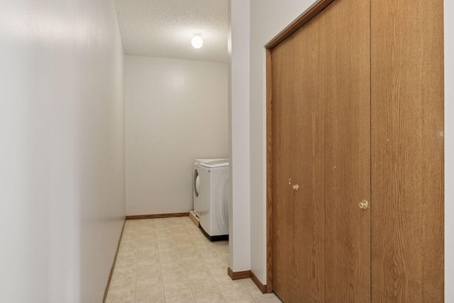 clothes washing area with baseboards, washing machine and dryer, light floors, laundry area, and a textured ceiling