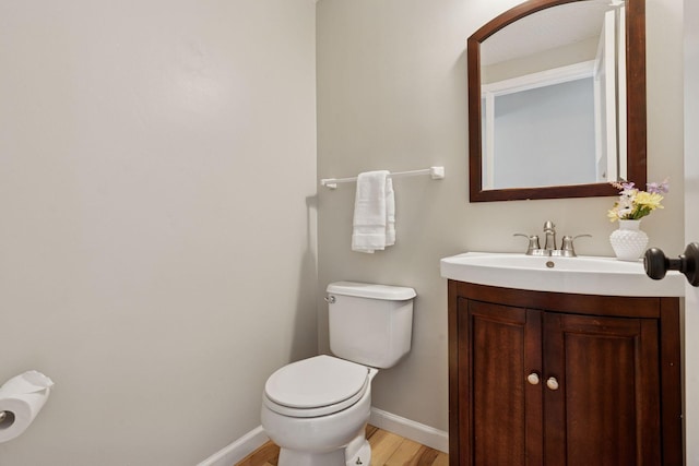 bathroom with toilet, vanity, baseboards, and wood finished floors