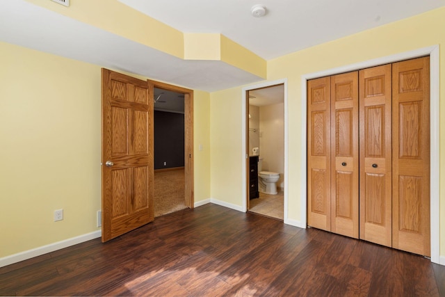 unfurnished bedroom with a closet, ensuite bathroom, baseboards, and dark wood-style flooring