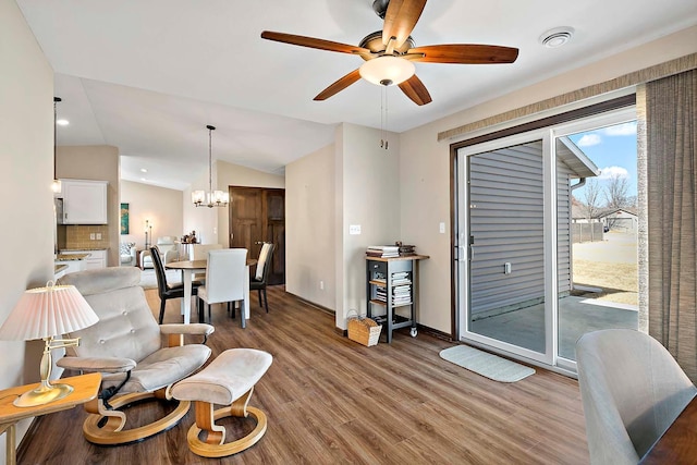 living area featuring vaulted ceiling, ceiling fan with notable chandelier, wood finished floors, and baseboards