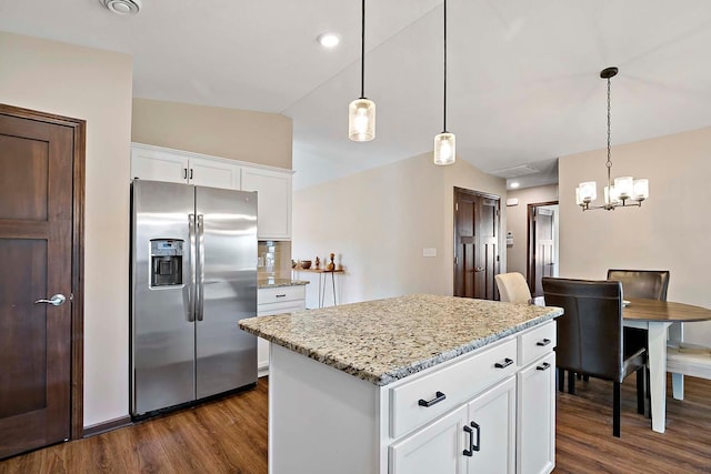 kitchen with light stone counters, stainless steel fridge, hanging light fixtures, and dark wood-style flooring
