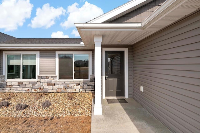 doorway to property with stone siding and roof with shingles