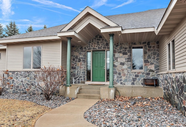 view of exterior entry featuring stone siding and a shingled roof