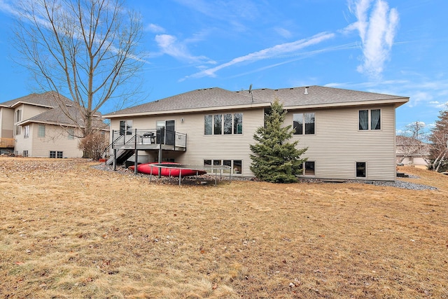 back of property with stairway, a trampoline, and roof with shingles