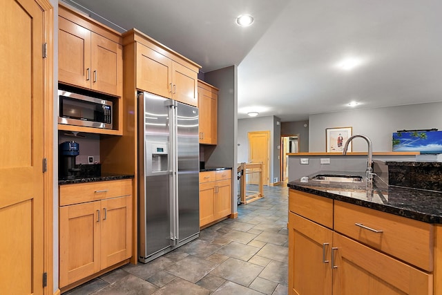 kitchen with a sink, dark stone countertops, stone finish flooring, recessed lighting, and stainless steel appliances