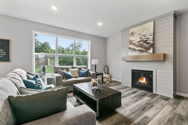 living area with a large fireplace, recessed lighting, wood finished floors, and baseboards