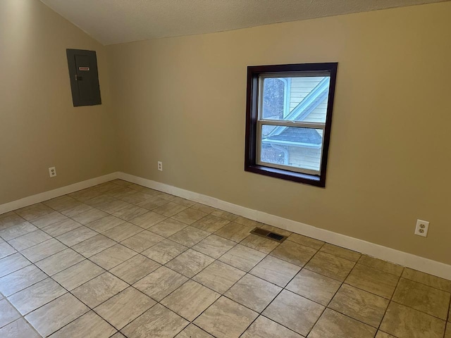 empty room featuring light tile patterned floors, electric panel, baseboards, visible vents, and vaulted ceiling