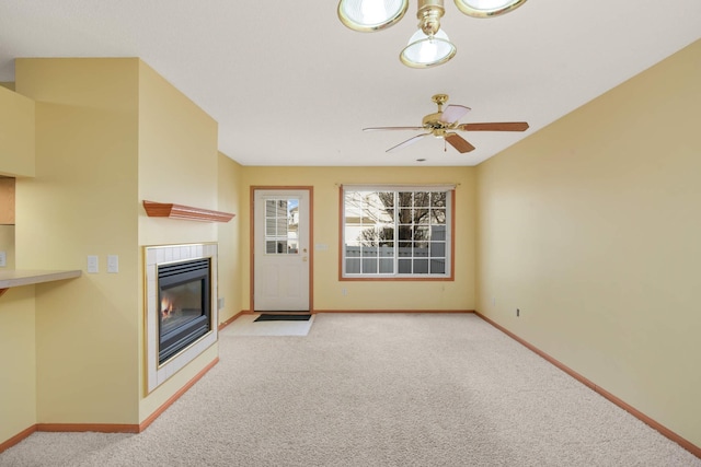 unfurnished living room with baseboards, carpet flooring, ceiling fan, and a tiled fireplace