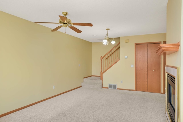 unfurnished living room with ceiling fan with notable chandelier, carpet floors, visible vents, baseboards, and stairway