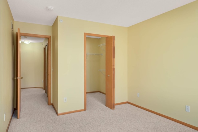 unfurnished bedroom featuring light carpet, visible vents, baseboards, a closet, and a walk in closet