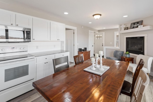 interior space with stainless steel microwave, recessed lighting, a kitchen breakfast bar, electric range, and white cabinetry