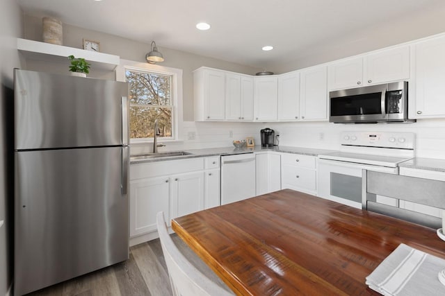 kitchen featuring decorative backsplash, appliances with stainless steel finishes, wood finished floors, white cabinets, and a sink