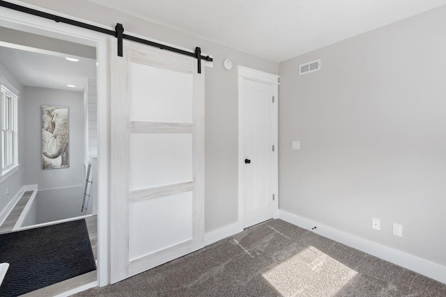 unfurnished bedroom with dark colored carpet, visible vents, a barn door, and baseboards