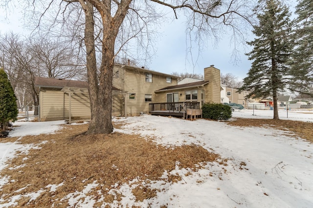 snow covered house featuring a garage, a chimney, a deck, and fence