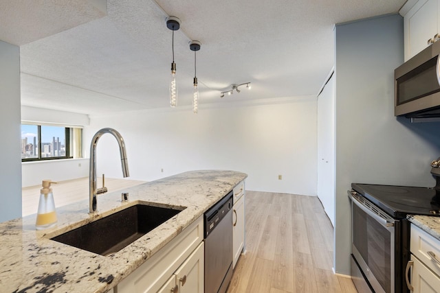 kitchen with light stone counters, a sink, stainless steel appliances, a textured ceiling, and light wood-type flooring