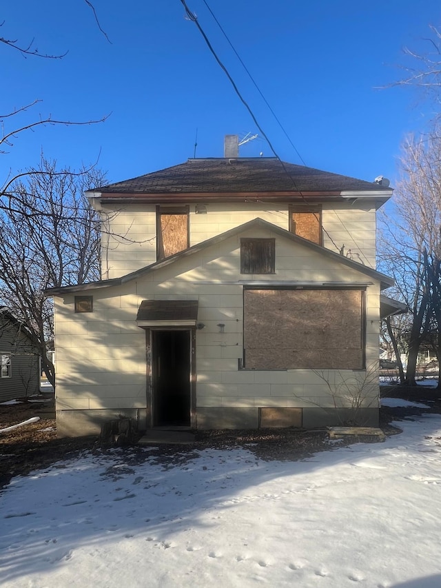 snow covered back of property featuring a chimney