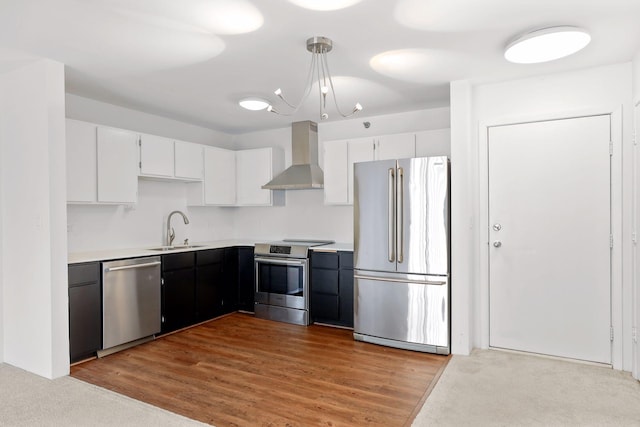 kitchen featuring wall chimney exhaust hood, stainless steel appliances, light countertops, white cabinetry, and a sink