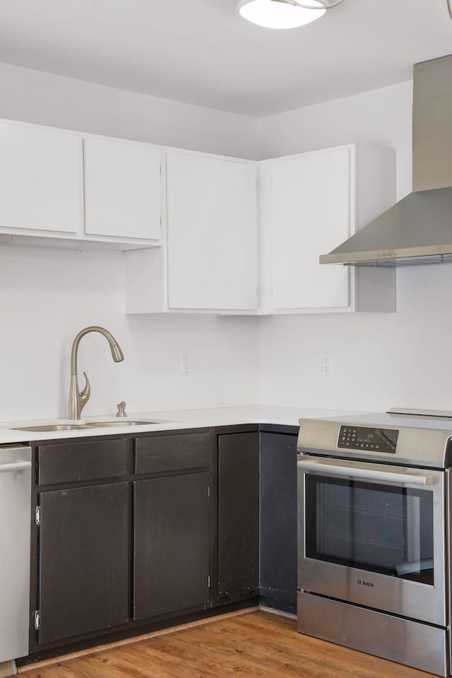 kitchen with wall chimney exhaust hood, appliances with stainless steel finishes, wood finished floors, white cabinetry, and a sink