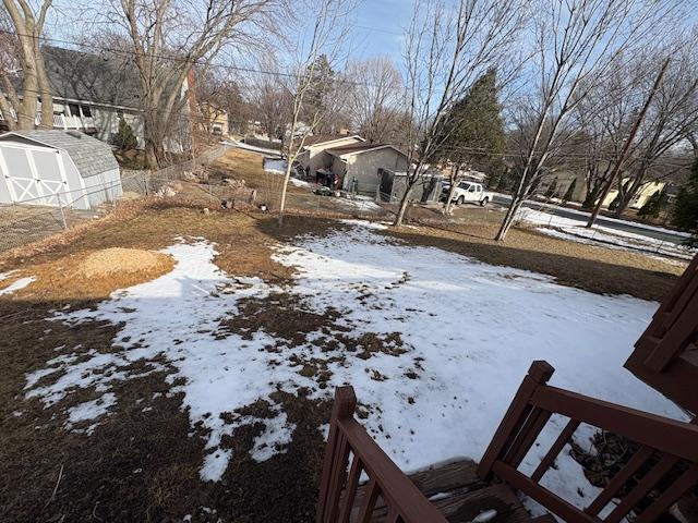 yard covered in snow featuring a storage shed, an outdoor structure, and a residential view