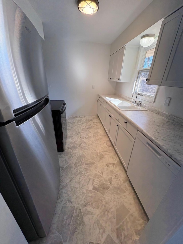 kitchen featuring dishwasher, light countertops, freestanding refrigerator, white cabinetry, and a sink