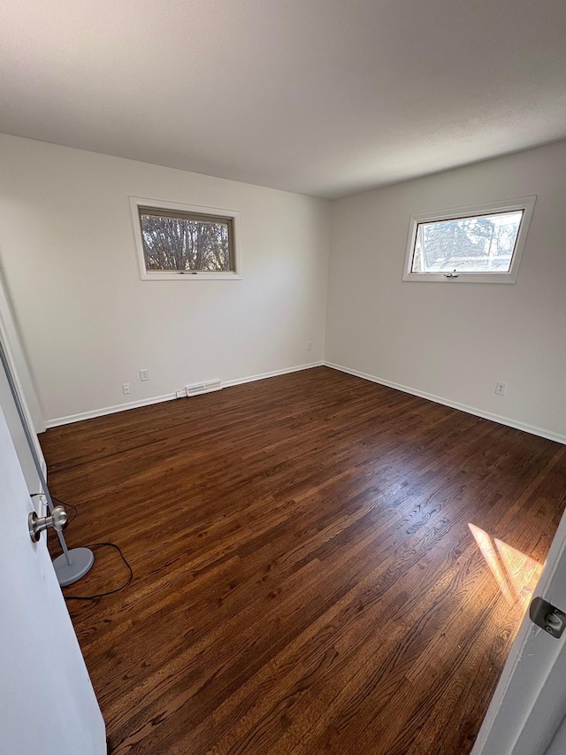 spare room featuring visible vents, baseboards, and dark wood-style flooring