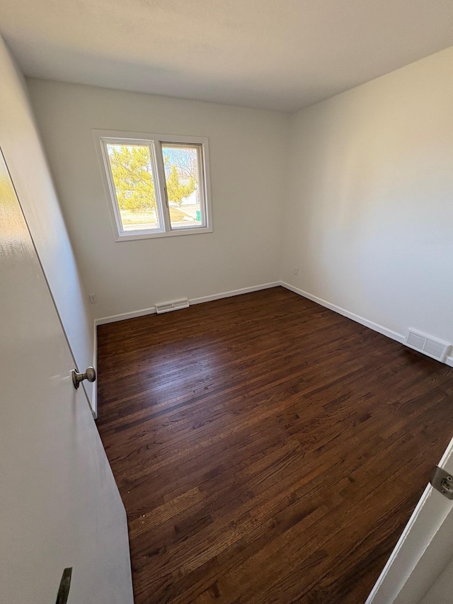 spare room featuring dark wood-type flooring, baseboards, and visible vents