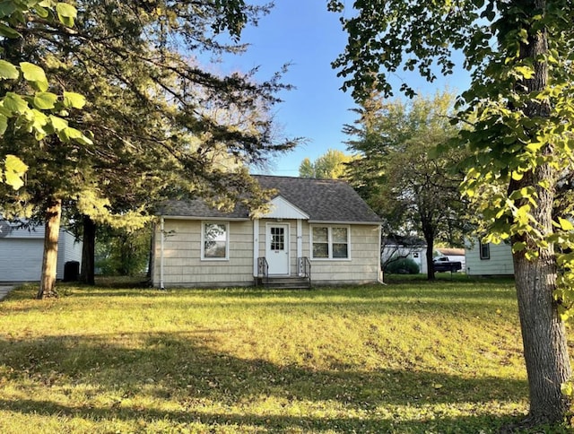 view of front facade with entry steps, a shingled roof, and a front lawn